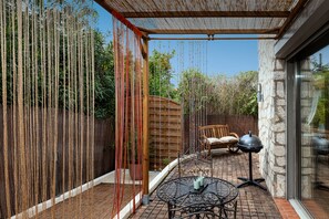 A patio with a round metal table, a wooden bench, and a barbecue grill.