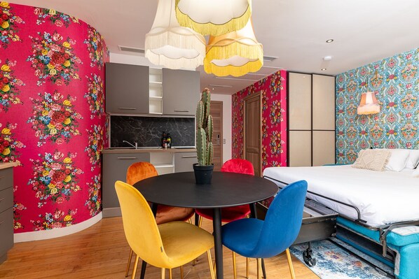 A modern room with a round table, colorful chairs, a bed, and a kitchen area.