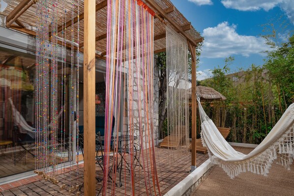 A wooden structure with a thatched roof, a hammock, and a hanging beaded curtain.