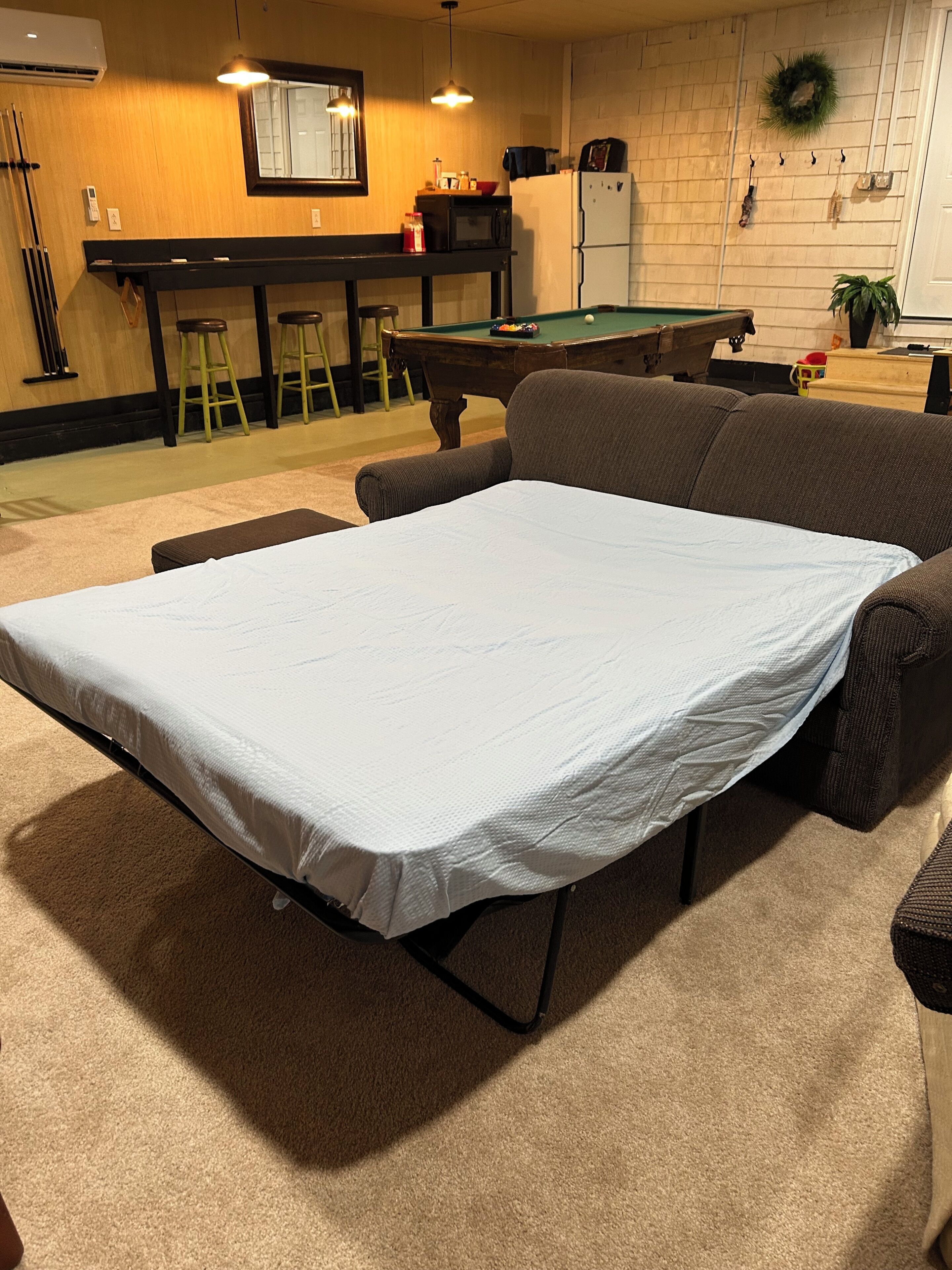 Et værelse med billardbord, sofa, barområde og ping pong-bord.