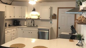 Una cocina moderna con armarios blancos, una isla central con sillas, un ventilador de techo y una estufa empotrada.