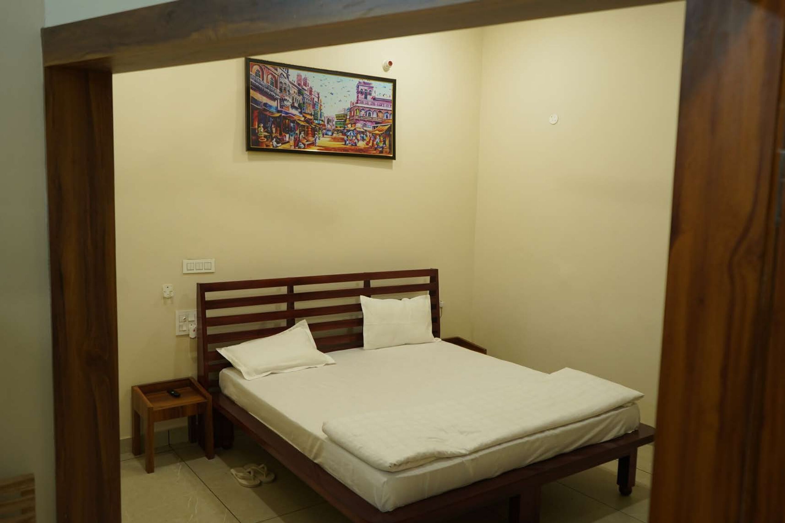 A bedroom with a wooden bed, a small bedside table, and a wall-mounted painting.