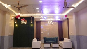A modern lobby with a reception desk, two sofas, a chandelier, ceiling fans, and a neon sign. - Maharaja Hotel and Restaurant (Ratia)