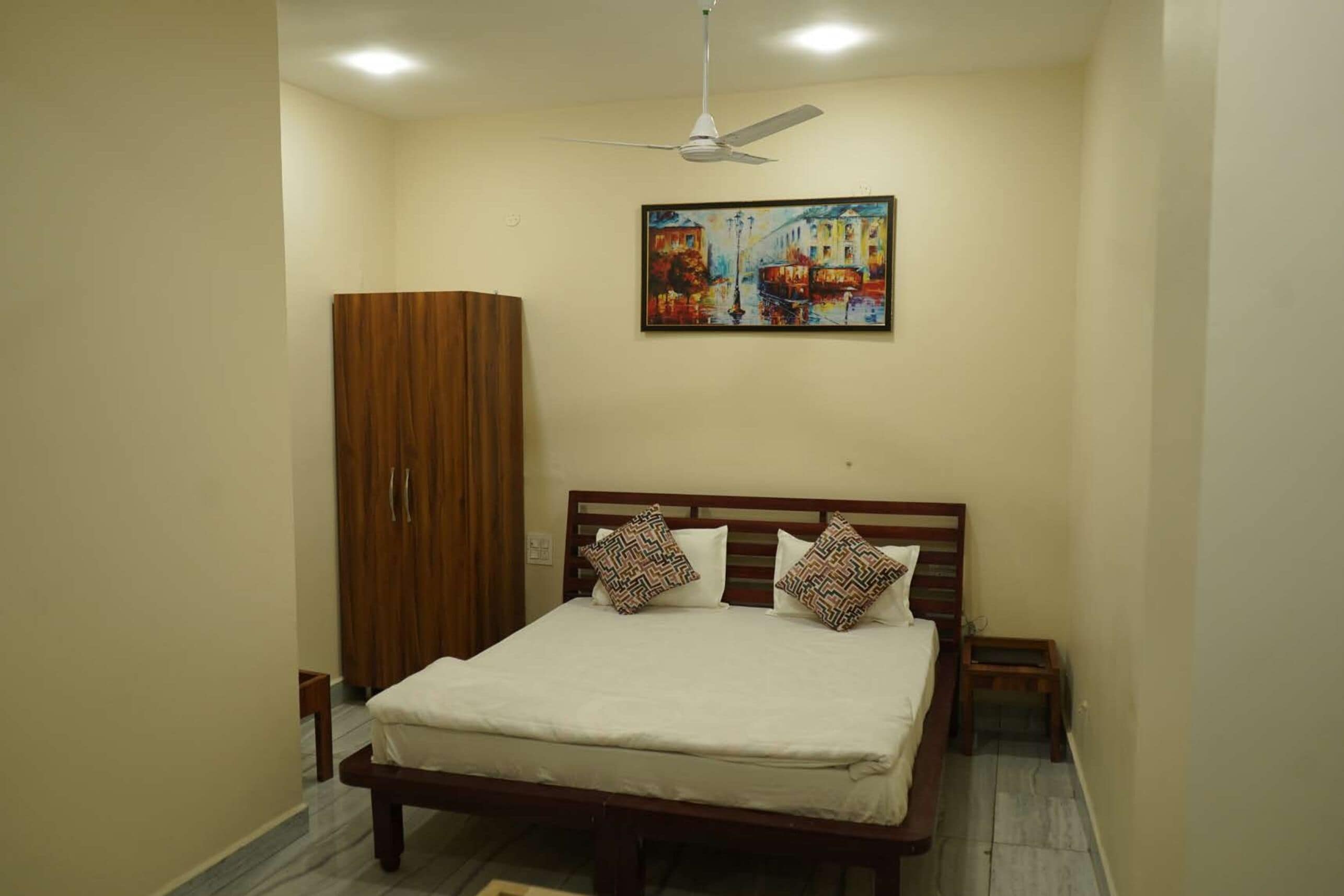 A bedroom with a bed, a wardrobe, a ceiling fan, and a painting on the wall.