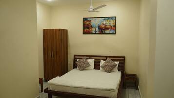 A bedroom with a bed, a wardrobe, a ceiling fan, and a painting on the wall.