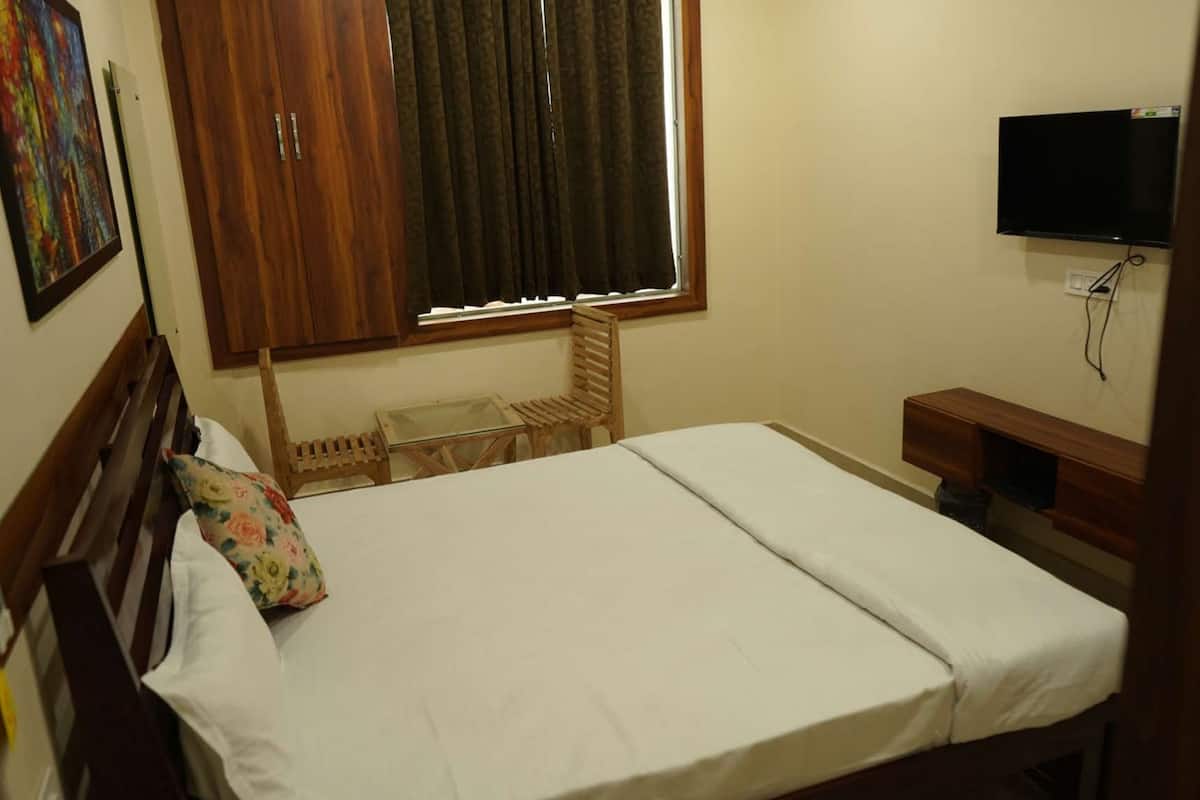 A bedroom with a bed, a wooden wardrobe, a television, and a window with curtains.