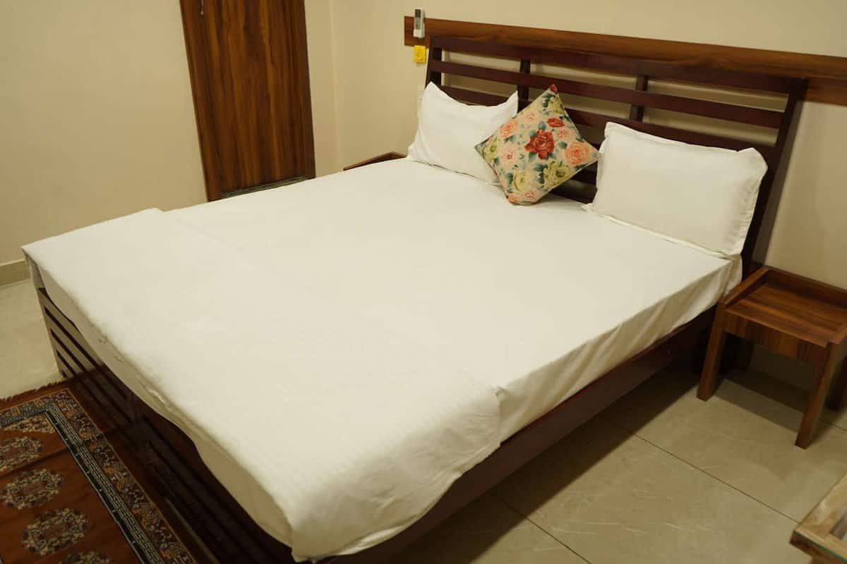 A neatly made bed with white linens, a wooden headboard, and a floral pillow. There is a small wooden nightstand beside the bed.