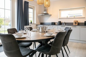 A modern kitchen with a dining table set for six, a large window with curtains, and a built-in stove.