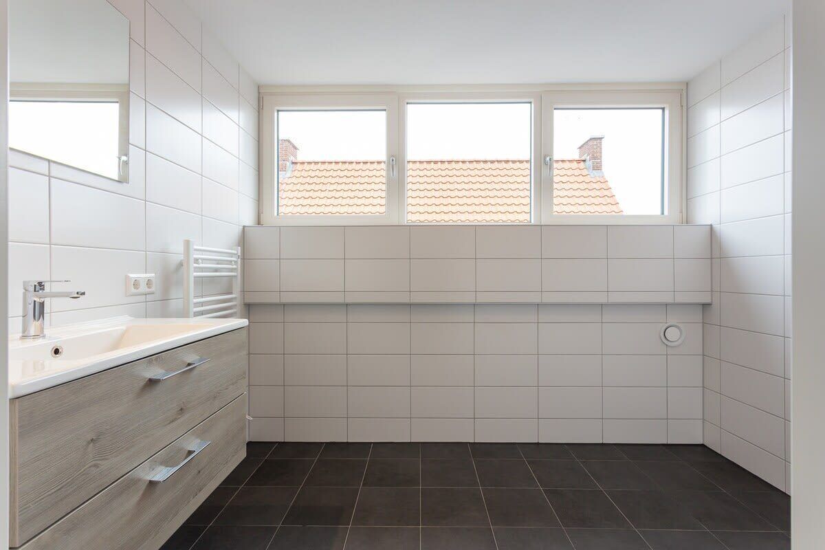 Une salle de bain moderne avec un meuble-lavabo blanc, une fenêtre et un sol carrelé.