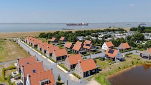 Zona residencial con casas de techos rojos, una masa de agua y barcos a lo lejos.