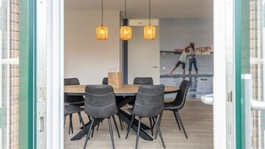 An open-plan dining area with a wooden table and black chairs, a hanging light fixture, and a mural of a beach scene in the background.