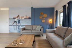 A living room with a sofa, a coffee table, and a wall mural depicting two people on a beach.
