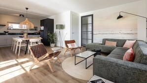 Una sala de estar moderna con un sofá, sillas, una mesa de centro y vistas al mar a través de un ventanal grande.