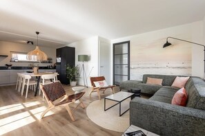 Un salon moderne avec un canapé gris, une table basse et un coin repas comprenant une table et des chaises blanches.