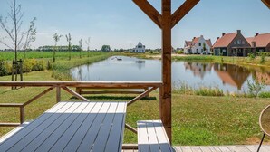 Una terraza de madera con una mesa y sillas que da a un río tranquilo y casas.