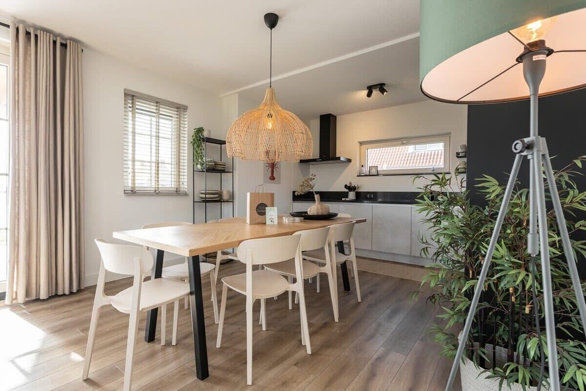 Ein moderner Essbereich mit einem Holztisch, weißen Stühlen, einer Pendelleuchte und einem Blumentopf.