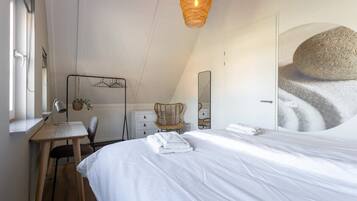 A bedroom with a bed, a desk, a chair, a hanging light fixture, and a large mirror.