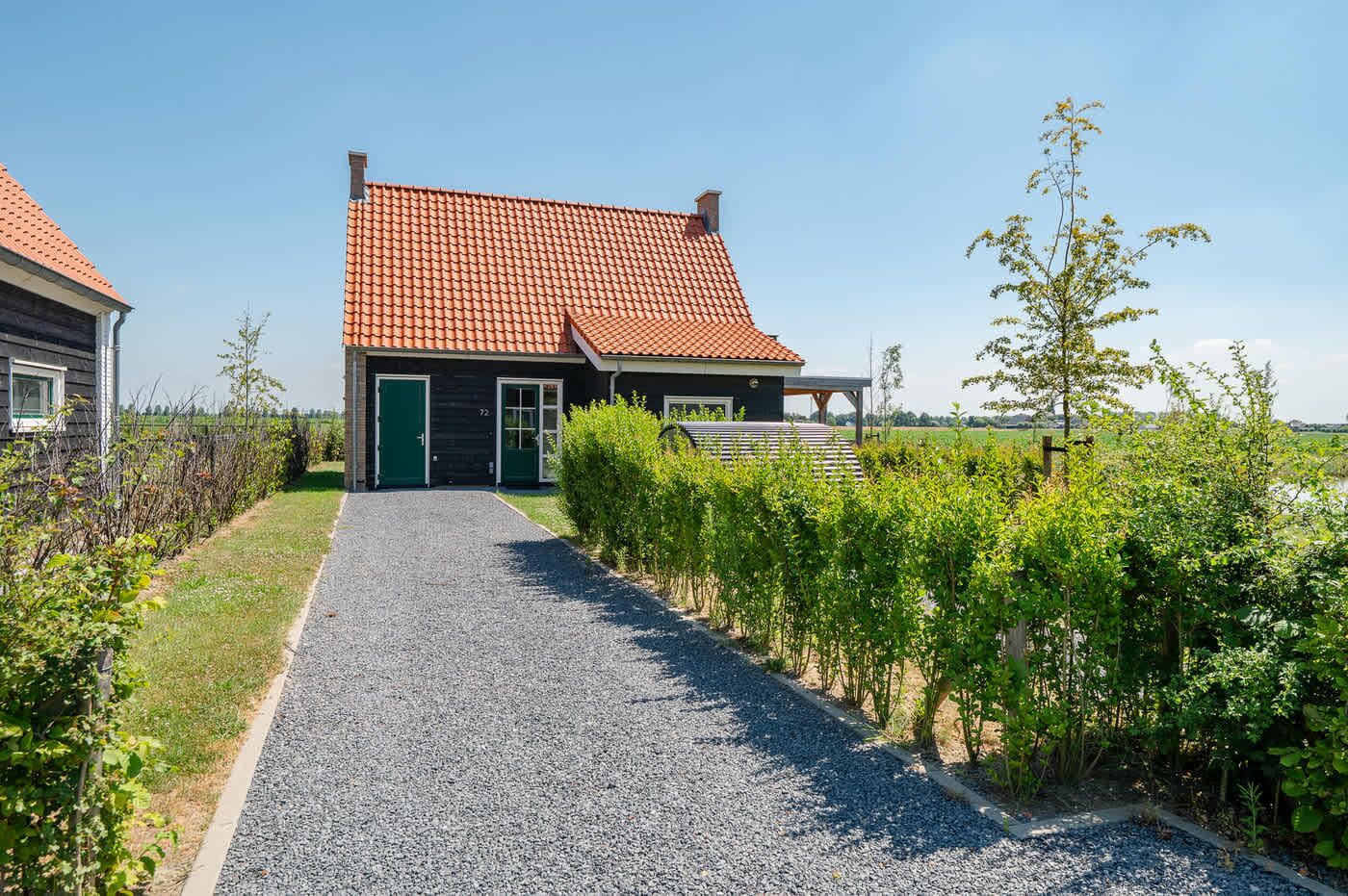 Een huis met een rode dakpan, een grindpad en een groene haag.