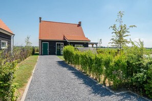 A house with a red-tiled roof, a gravel driveway, and a green hedge.