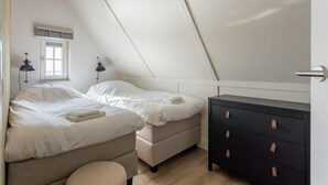 Un dormitorio con techo inclinado, dos camas, un aparador y una ventana con persianas.