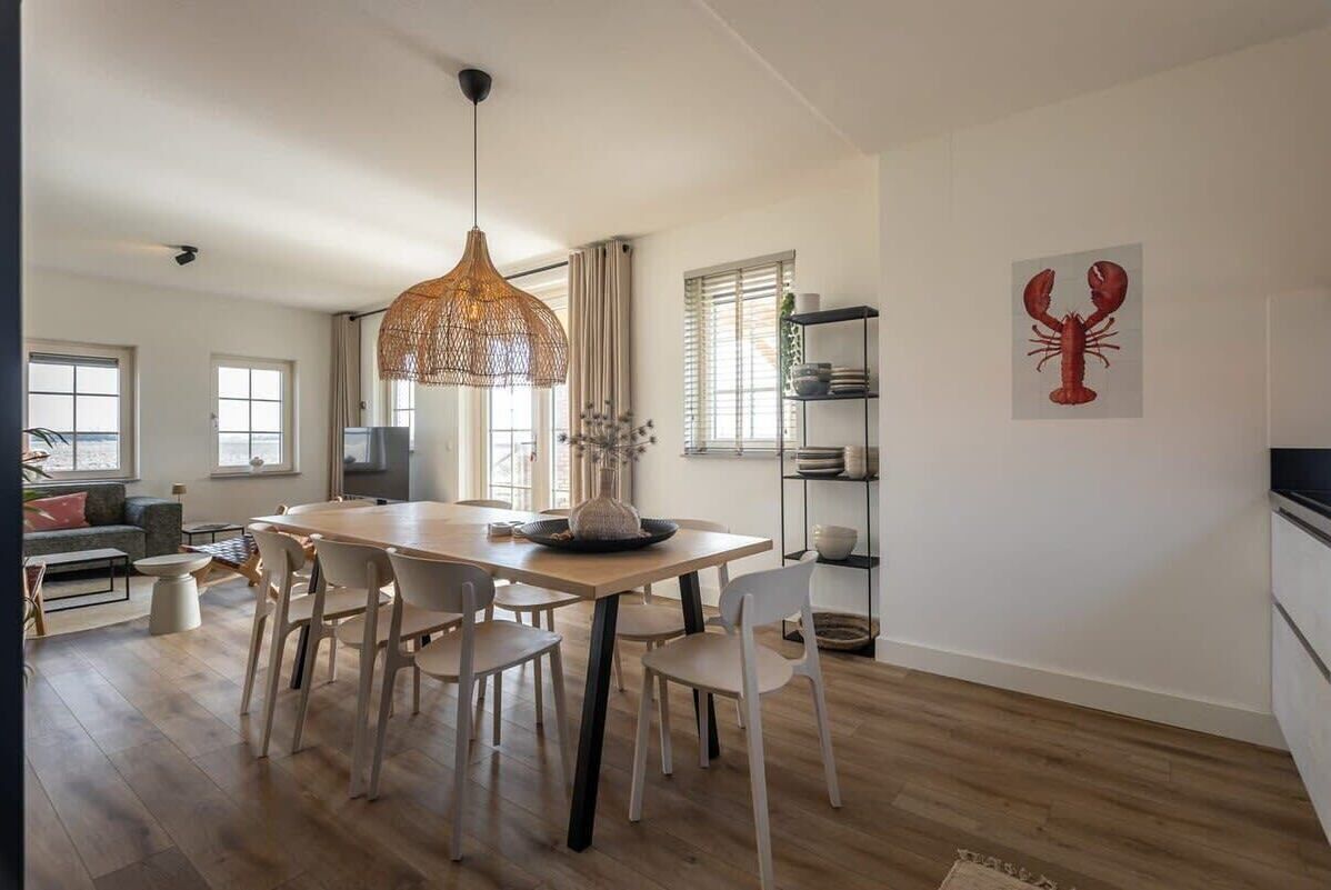 Un espace de repas moderne avec une table et des chaises en bois, un luminaire suspendu et une œuvre d’art représentant un homard accrochée au mur.
