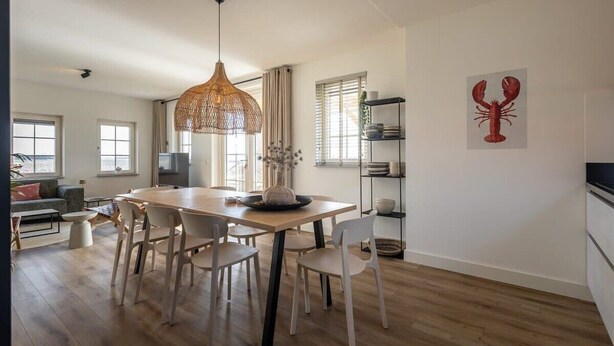 Un comedor moderno con una mesa y sillas de madera, una lámpara colgante y una obra de arte de langosta en la pared.
