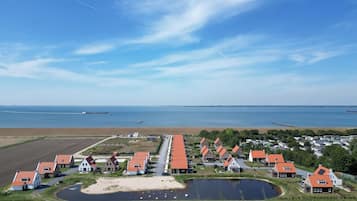 A coastal village with houses featuring red roofs, a small pond, and a view of the sea and distant ships.