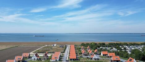 A coastal village with houses featuring red roofs, a small pond, and a view of the sea and distant ships.