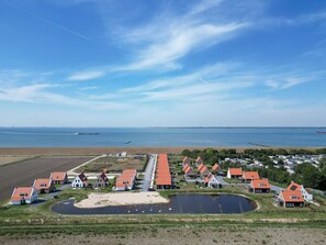 Un pueblo costero con casas de techos rojos, un pequeño estanque y vistas al mar y barcos a lo lejos.