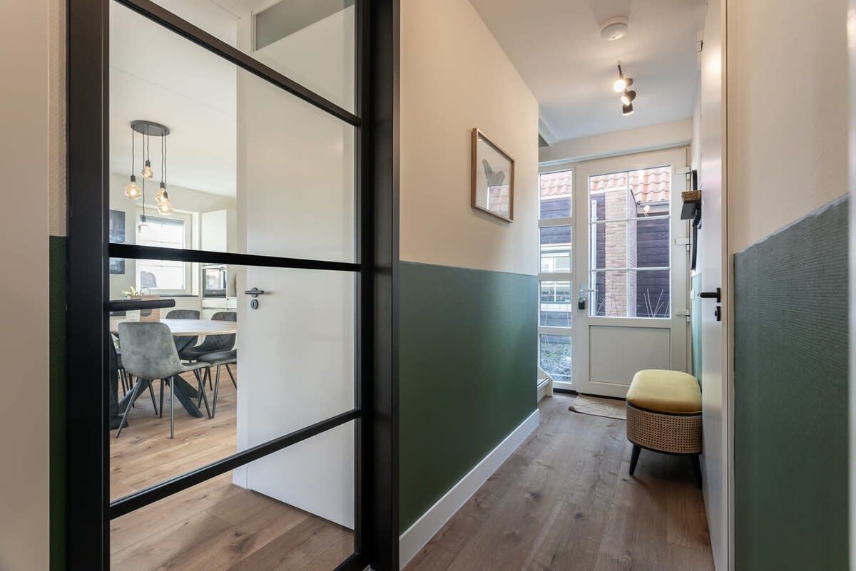 A hallway with a dining area visible through a glass door, a wicker chair, and a framed picture on the wall.