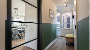 A hallway with a dining area visible through a glass door, a wicker chair, and a framed picture on the wall.