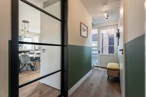 A hallway with a dining area, a wicker chair, and a door leading to a balcony.