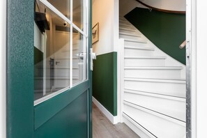 Corredor com porta verde, paredes brancas e escada com degraus brancos.