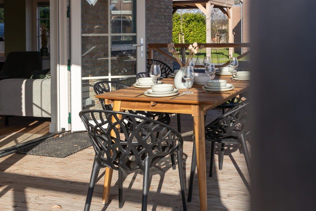 Un espace extérieur aménagé pour les repas, avec une table en bois pour quatre personnes, entourée de chaises noires, et une porte vitrée donnant sur un patio.