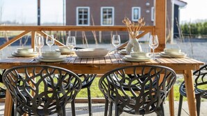 Mesa de madera preparada para cuatro personas, con platos, tazones y copas de vino blancos, rodeada de sillas negras.