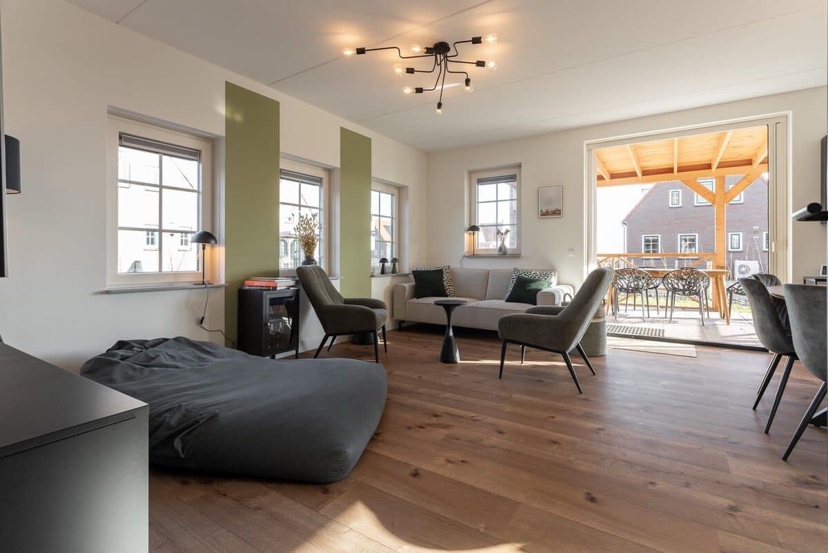 A modern living room with a sofa, chairs, a coffee table, and a fireplace. There are large windows and a view of the outside.