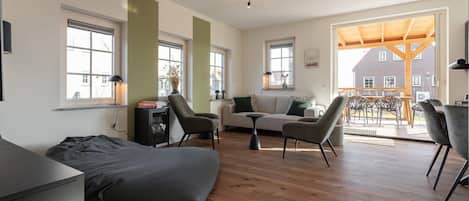 Un salon moderne avec un canapé, des fauteuils, une table basse et une cheminée. De grandes fenêtres offrent une vue sur l’extérieur.