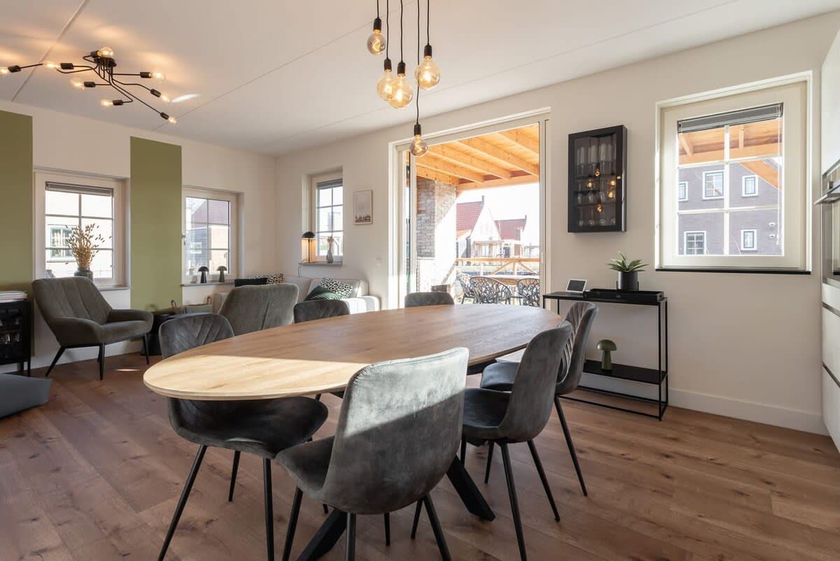 Un vaste espace dédié à la salle à manger, avec une longue table en bois et des chaises modernes, un lustre et de grandes fenêtres offrant une vue sur l’extérieur.