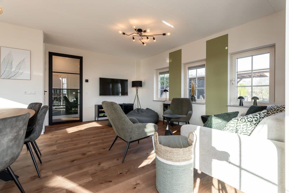A modern living room with a wooden floor, grey sofas, a TV, and a large window.
