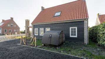 A house with a red-tiled roof, a wooden exterior, and a small shed in the front yard.
