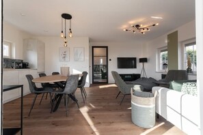 Una sala de estar moderna con comedor, televisor y cocina al fondo.