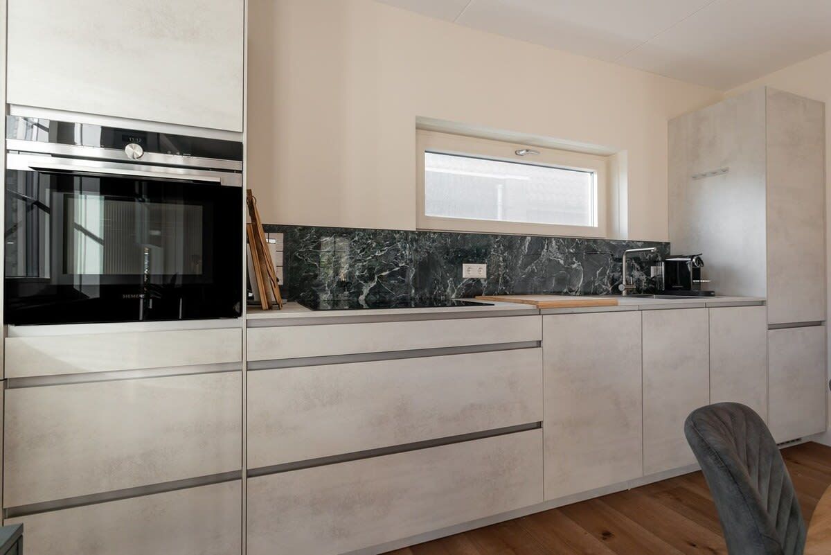 A modern kitchen with a built-in oven, a window above the countertop, and a marble backsplash.