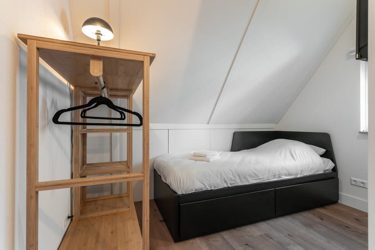 A bedroom with a black bed, wooden wardrobe, and a hanging light fixture.