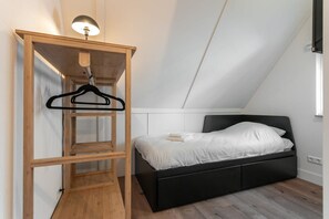 Un dormitorio con una cama negra, un armario de madera y una lámpara colgante.