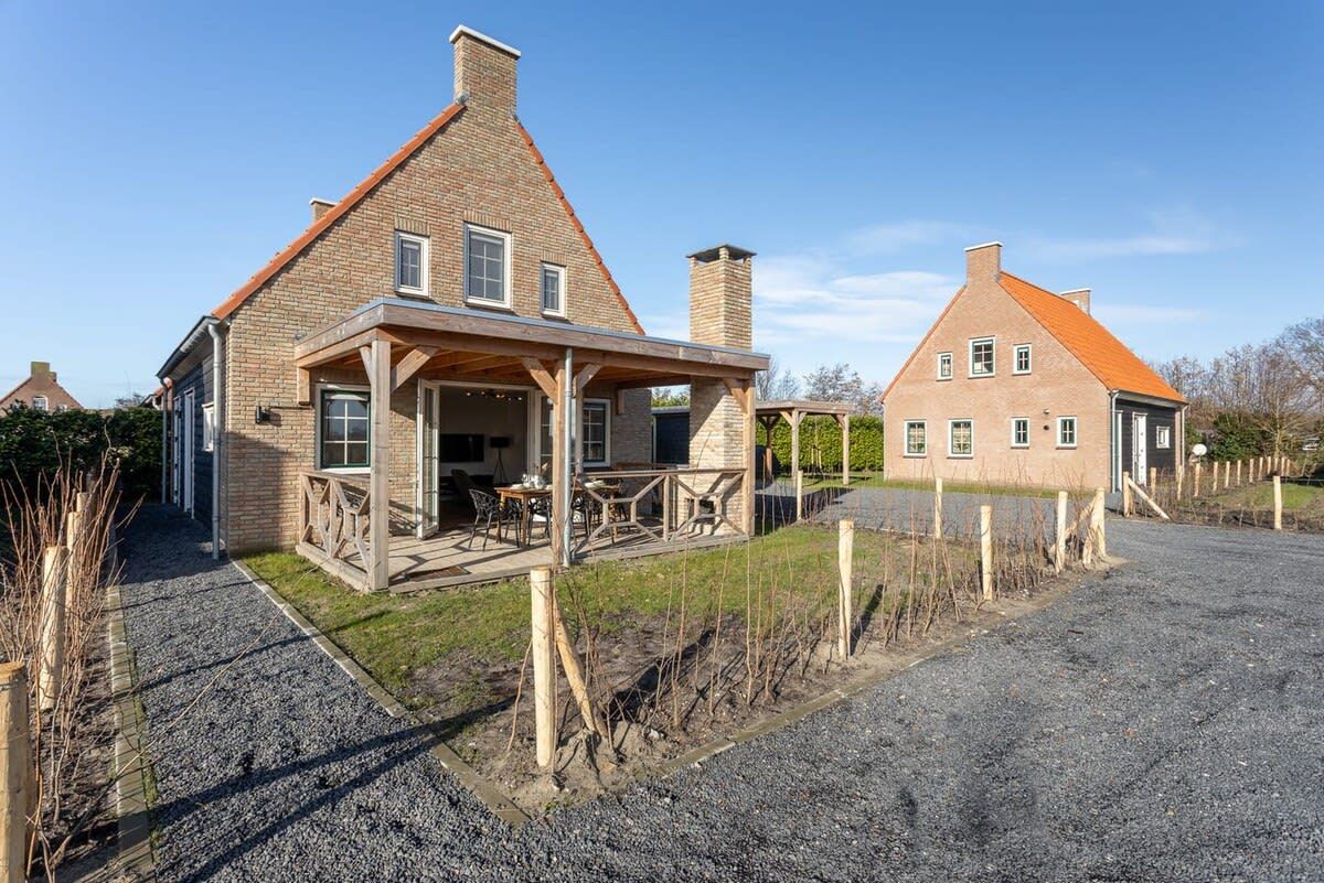 A two-story house with a stone facade, a wooden porch, and a gravel driveway.