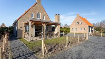 A two-story house with a stone facade, a wooden porch, and a gravel driveway.