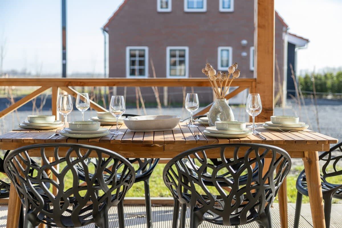 An outdoor dining area with a wooden table set for four, surrounded by black metal chairs.