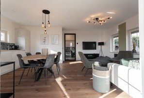 A modern living room with a dining area, a TV, and a kitchen in the background.