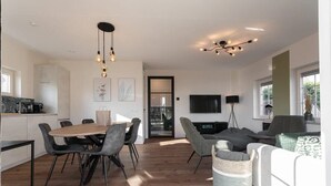 Una sala de estar moderna con comedor, televisor y cocina al fondo.