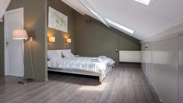 A bedroom with a skylight, a bed, bedside lamps, and a radiator.